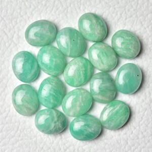 May include: A collection of 15 oval-shaped green amazonite gemstones. The stones are smooth and polished, with a light green color and white streaks.