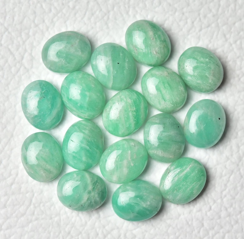 May include: A collection of 15 oval-shaped green amazonite gemstones. The stones are smooth and polished, with a light green color and white streaks.