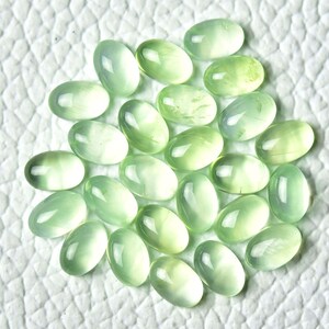 May include: A collection of 20 oval-shaped green gemstones. The stones are smooth and polished, with a translucent appearance.