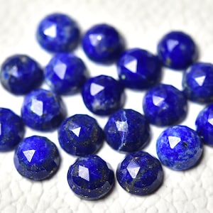 May include: A collection of 17 faceted lapis lazuli gemstones, each with a deep blue color and flecks of gold pyrite. The stones are arranged in a random pattern on a white surface.