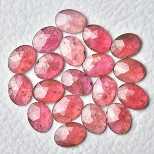 May include: A collection of 18 oval-shaped, faceted, pink gemstones. The stones have a translucent appearance with a slight shimmer.