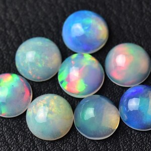Pode incluir: Uma cole&ccedil;&atilde;o de oito caboch&otilde;es de opala redondos e iridescentes. As opalas s&atilde;o de v&aacute;rios tons de azul, verde, rosa e branco.