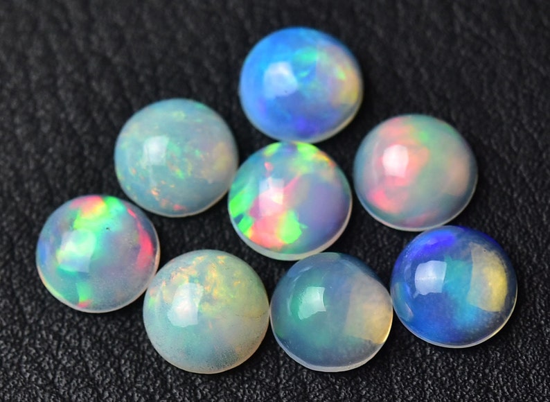 Pode incluir: Uma cole&ccedil;&atilde;o de oito caboch&otilde;es de opala redondos e iridescentes. As opalas s&atilde;o de v&aacute;rios tons de azul, verde, rosa e branco.