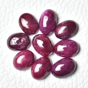 May include: Nine oval-shaped, polished ruby gemstones in various shades of pink and red.