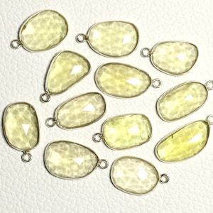 Könnte beinhalten: Zwölf gelbe Edelstein-Anhänger mit silbernen Sprungringen. Die Edelsteine sind facettiert und haben eine durchscheinende Optik.