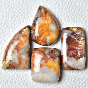May include: Four cabochon cut gemstone cabochons in various shapes and sizes. The stones are a mix of white, brown, orange, and red with a marbled pattern.
