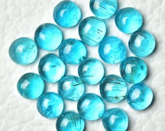 May include: A collection of twenty round, polished gemstones. The gems are a vibrant, translucent turquoise blue with internal striations. They are scattered on a white surface, showcasing their color and clarity. The gemstones are likely for jewelry making or collecting.