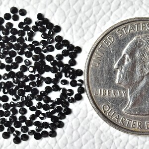 May include: A pile of small, black, round, faceted gemstones, next to a US quarter for size comparison.