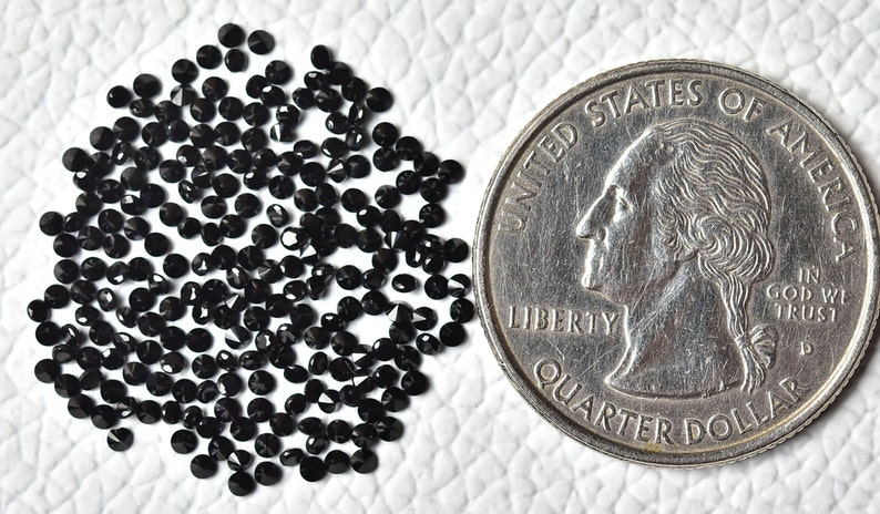 May include: A pile of small, black, round, faceted gemstones, next to a US quarter for size comparison.