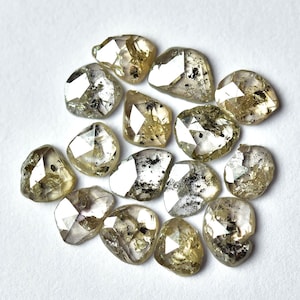 May include: A collection of 15 rough, unpolished, light brown diamonds with a silvery sheen. The diamonds are faceted and have a variety of shapes and sizes.