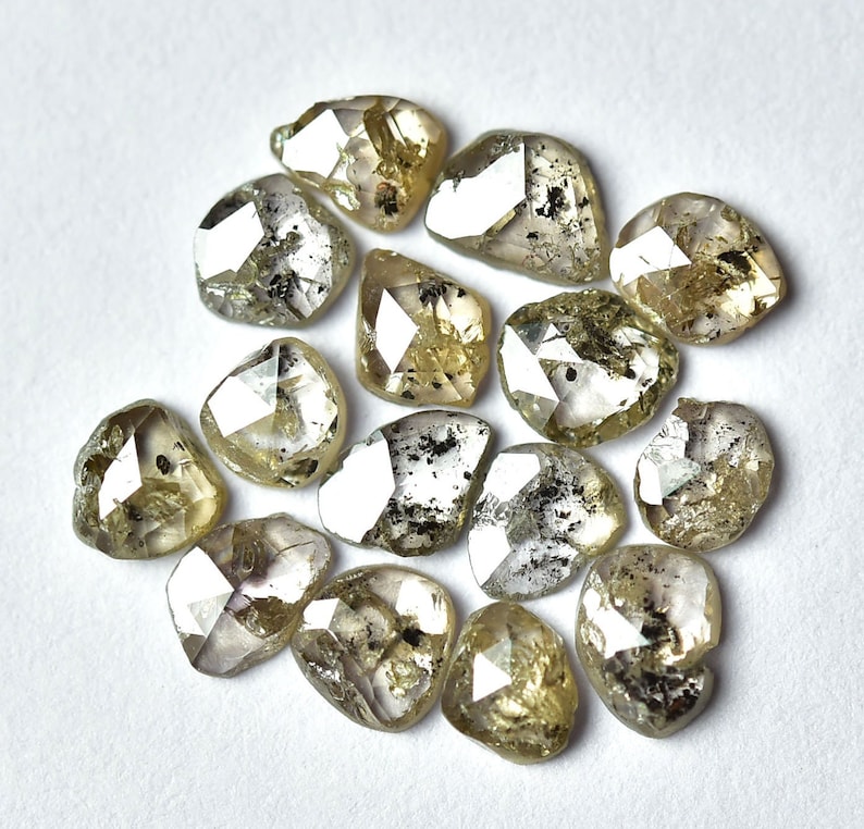 May include: A collection of 15 rough, unpolished, light brown diamonds with a silvery sheen. The diamonds are faceted and have a variety of shapes and sizes.