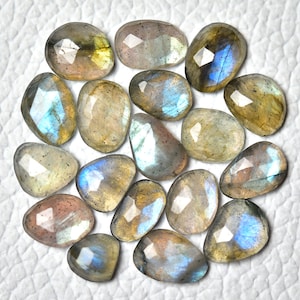 May include: A collection of 17 faceted labradorite gemstones in various shades of grey, blue, and green. The stones have a pearlescent sheen and are arranged in a loose pile.