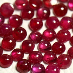May include: A strand of ruby red gemstones, each cabochon cut and polished to a smooth, rounded shape. The stones are arranged in a line, creating a visually appealing pattern.