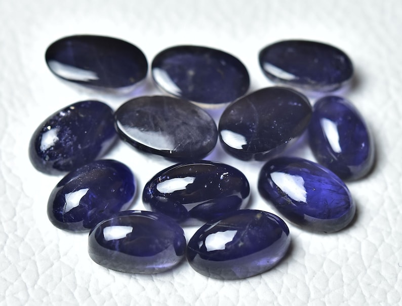 May include: A collection of ten oval-shaped, polished gemstones. The stones are a deep purple-blue colour and have a glossy finish.