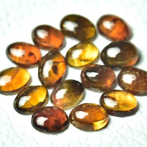 May include: A collection of 14 oval-shaped gemstones in shades of brown, orange, and yellow. The gemstones are smooth and polished, with a glossy finish.
