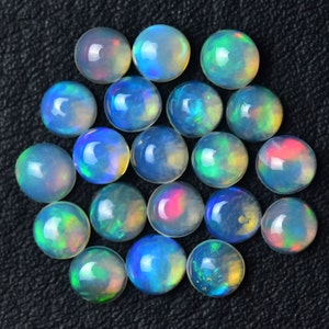 May include: A collection of 20 round opal cabochons in various shades of blue, green, and white. The cabochons are arranged in a circular pattern on a black surface.