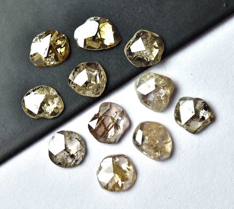 May include: A collection of 11 rough, uncut, natural diamonds. The diamonds are various shades of brown and yellow and have a faceted, irregular shape.
