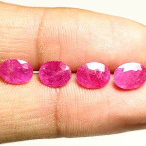 Può includere: Quattro pietre preziose rosa di forma ovale, probabilmente rubini, sono esposte su un dito.