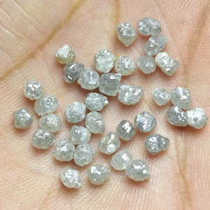 Puede incluir: Una colecci&oacute;n de peque&ntilde;os diamantes grises en bruto. Los diamantes son de varias formas y tama&ntilde;os, y est&aacute;n esparcidos en una mano.