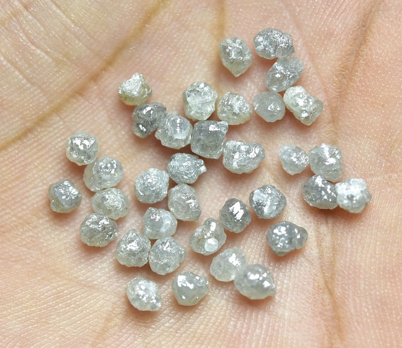 Puede incluir: Una colecci&oacute;n de peque&ntilde;os diamantes grises en bruto. Los diamantes son de varias formas y tama&ntilde;os, y est&aacute;n esparcidos en una mano.