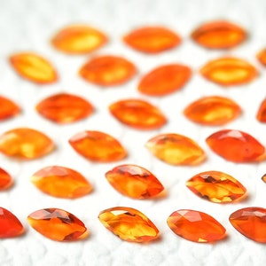 May include: A collection of 25 orange marquise-shaped gemstones arranged in a heart shape on a white surface.