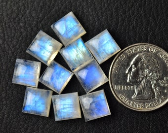 Könnte beinhalten: Zehn quadratische Mondstein-Cabochons, jeder mit einem blauen, irisierenden Schimmer. Die Steine sind in einem zufälligen Muster angeordnet und haben etwa die Größe einer US-amerikanischen 25-Cent-Münze.