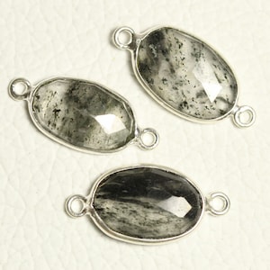 May include: Three silver oval-shaped pendants with clear quartz stones with black inclusions. The stones are faceted and have a silver bail on each end.