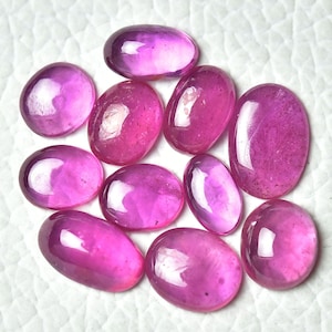 May include: A collection of ten oval-shaped pink gemstones. The gemstones are smooth and polished, with a slight sheen.