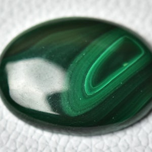 May include: A smooth, green malachite cabochon with swirling patterns. The stone has a polished, glossy finish.