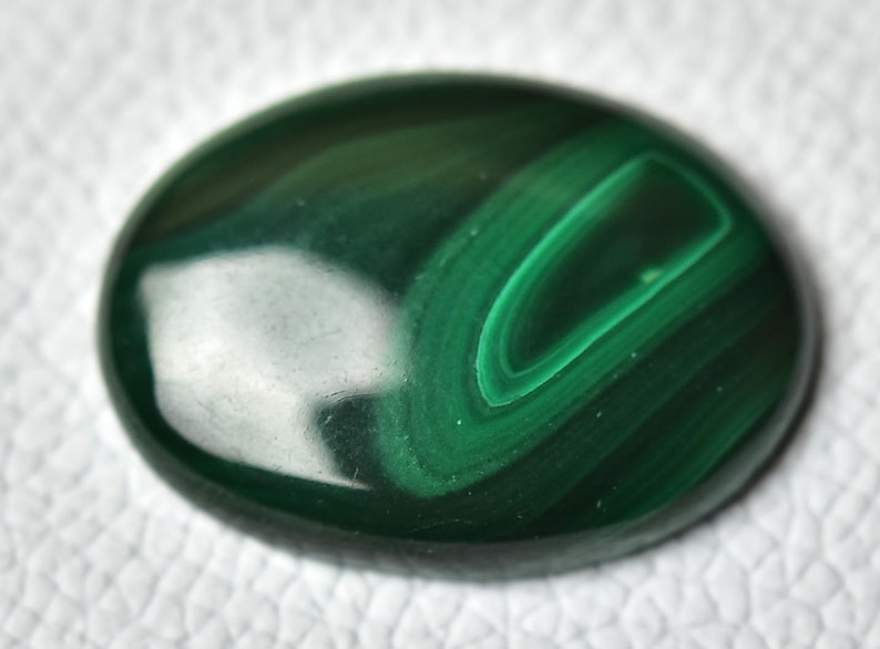 May include: A smooth, green malachite cabochon with swirling patterns. The stone has a polished, glossy finish.