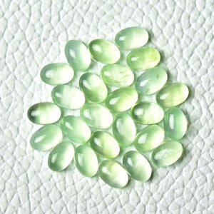 May include: A collection of 25 oval-shaped green gemstones. The stones are smooth and polished, with a translucent appearance.