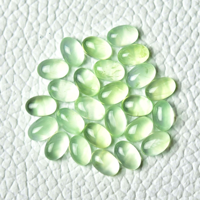 May include: A collection of 25 oval-shaped green gemstones. The stones are smooth and polished, with a translucent appearance.