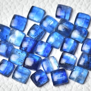 Peut inclure: Une collection de cabochons de cyanite bleue, taillés en forme carrée. Les pierres ont une couleur bleu clair avec un aspect blanc et nuageux.