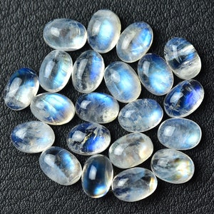 May include: A collection of oval-shaped moonstone cabochons with a milky white color and iridescent blue flashes.