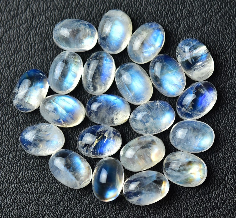 May include: A collection of oval-shaped moonstone cabochons with a milky white color and iridescent blue flashes.