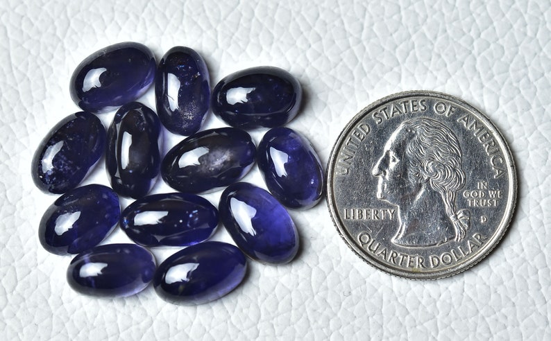May include: A group of 12 oval-shaped, dark blue gemstones, each approximately the size of a UK 20 pence coin.