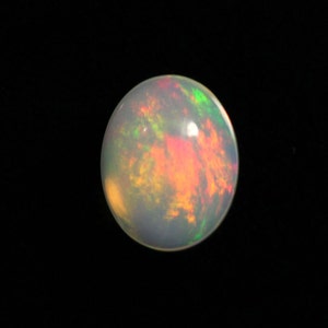 Può includere: Una pietra preziosa di opale rotonda e bianca con riflessi iridescenti verdi, arancioni e rossi.