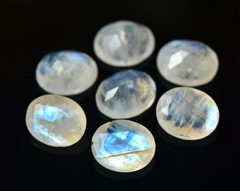 May include: Seven oval-shaped moonstone cabochons with a iridescent blue sheen. The stones are arranged in a circular pattern on a black background.