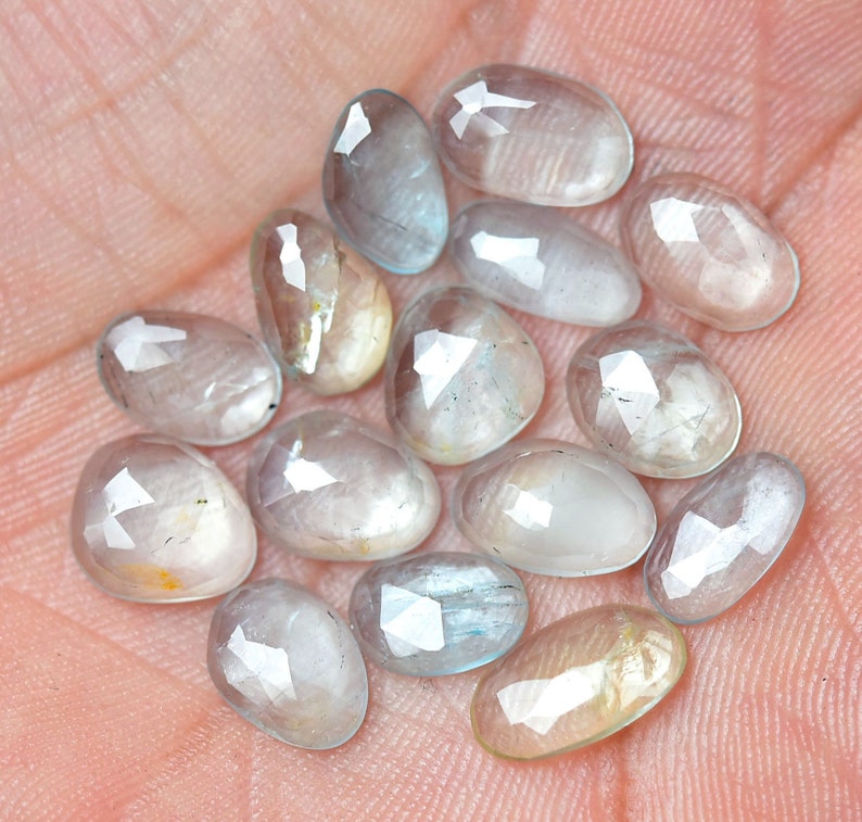 Puede incluir: Una colecci&oacute;n de 14 piedras preciosas ovaladas facetadas, transl&uacute;cidas, de color azul claro. Las piedras tienen una apariencia ligeramente nublada y est&aacute;n dispuestas en un mont&oacute;n suelto.