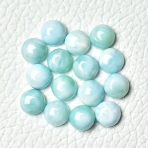 Puede incluir: Una colecci&oacute;n de 15 piedras preciosas redondas en cabuj&oacute;n de color azul claro y blanco. Las piedras preciosas tienen una superficie lisa y pulida y est&aacute;n dispuestas en un patr&oacute;n circular.