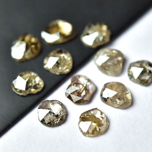 May include: A collection of ten faceted, rough-cut, brown diamonds. The diamonds are arranged on a black and white surface.