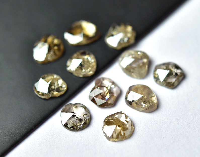 May include: A collection of ten faceted, rough-cut, brown diamonds. The diamonds are arranged on a black and white surface.