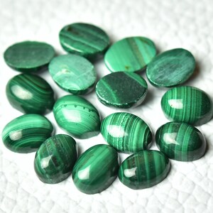 May include: A collection of 14 oval-shaped malachite cabochons in various shades of green. The stones have a smooth, polished finish and display intricate patterns of swirling green hues.