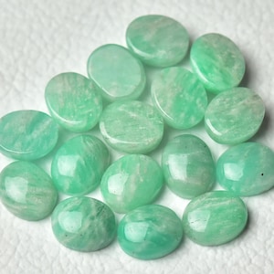 May include: A collection of 15 oval-shaped green gemstones, likely amazonite, arranged on a white surface. The stones are smooth and polished, with a variety of shades of green.