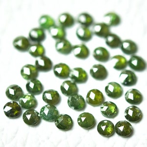 Pode incluir: Uma coleção de pedras preciosas verdes, facetadas e de forma oval. As pedras estão espalhadas sobre uma superfície branca.