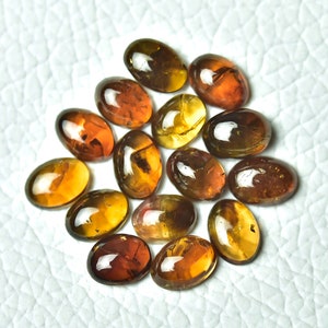 May include: A collection of 14 oval-shaped gemstones with a mix of brown, amber, and yellow hues. The stones have a translucent appearance and show some internal inclusions.