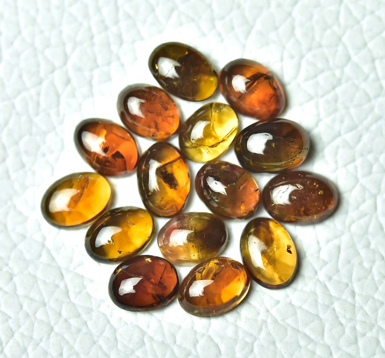 May include: A collection of 14 oval-shaped gemstones with a mix of brown, amber, and yellow hues. The stones have a translucent appearance and show some internal inclusions.