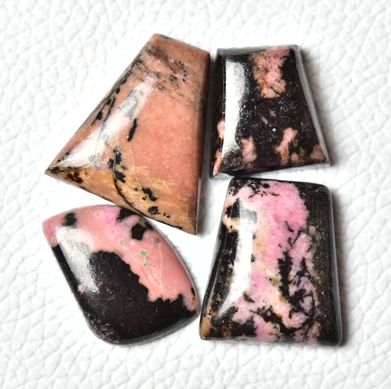 May include: Four pink and black cabochon gemstones with a polished finish. The stones are cut in different shapes and sizes.