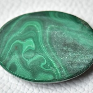 May include: A smooth, oval-shaped malachite stone with a green and white marbled pattern.