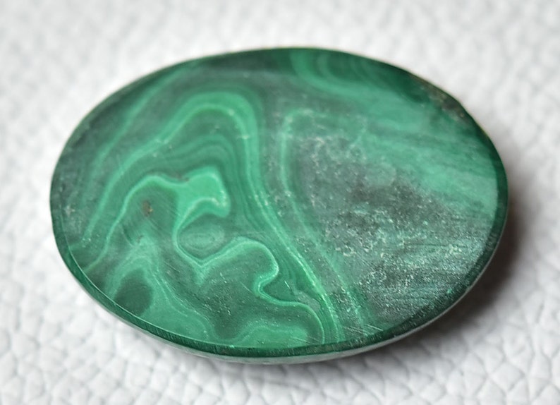 May include: A smooth, oval-shaped malachite stone with a green and white marbled pattern.